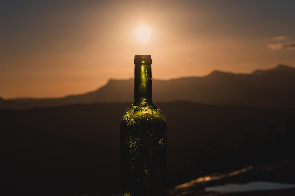 Bottiglia di vetro verde sul tavolo di legno marrone durante il tramonto