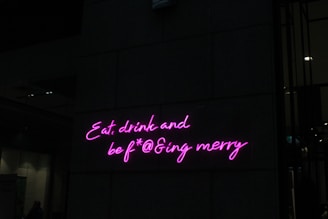 Neon pink letters form a playful and slightly irreverent phrase on a dark wall, adding a vibrant and humorous touch to the setting.