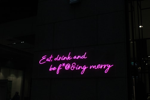 Neon pink letters form a playful and slightly irreverent phrase on a dark wall, adding a vibrant and humorous touch to the setting.