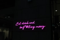 Neon pink letters form a playful and slightly irreverent phrase on a dark wall, adding a vibrant and humorous touch to the setting.