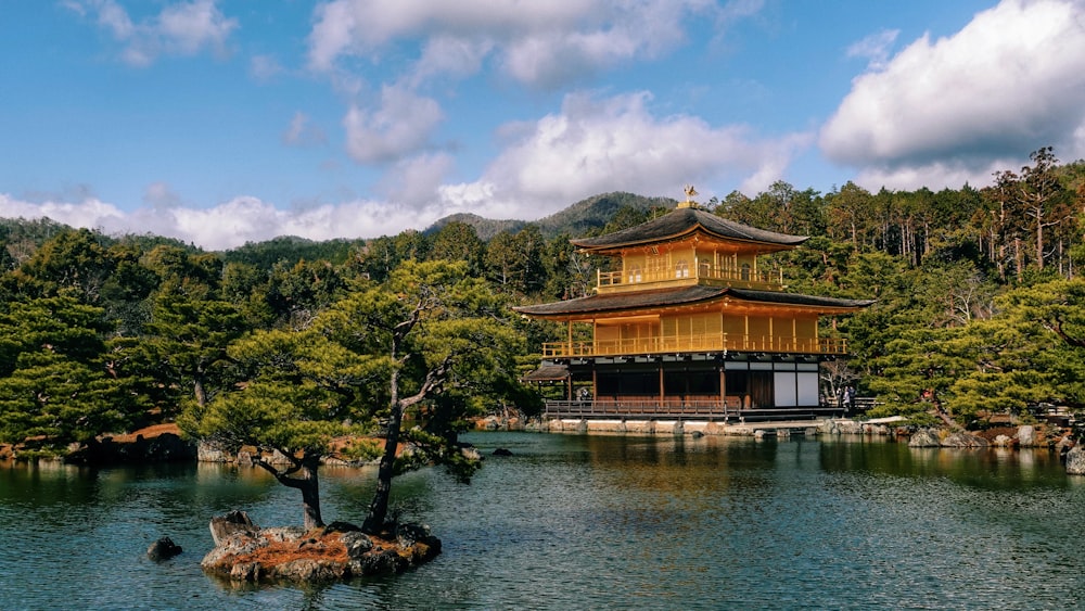 brown and white wooden house near body of water and green mountain under blue sky during