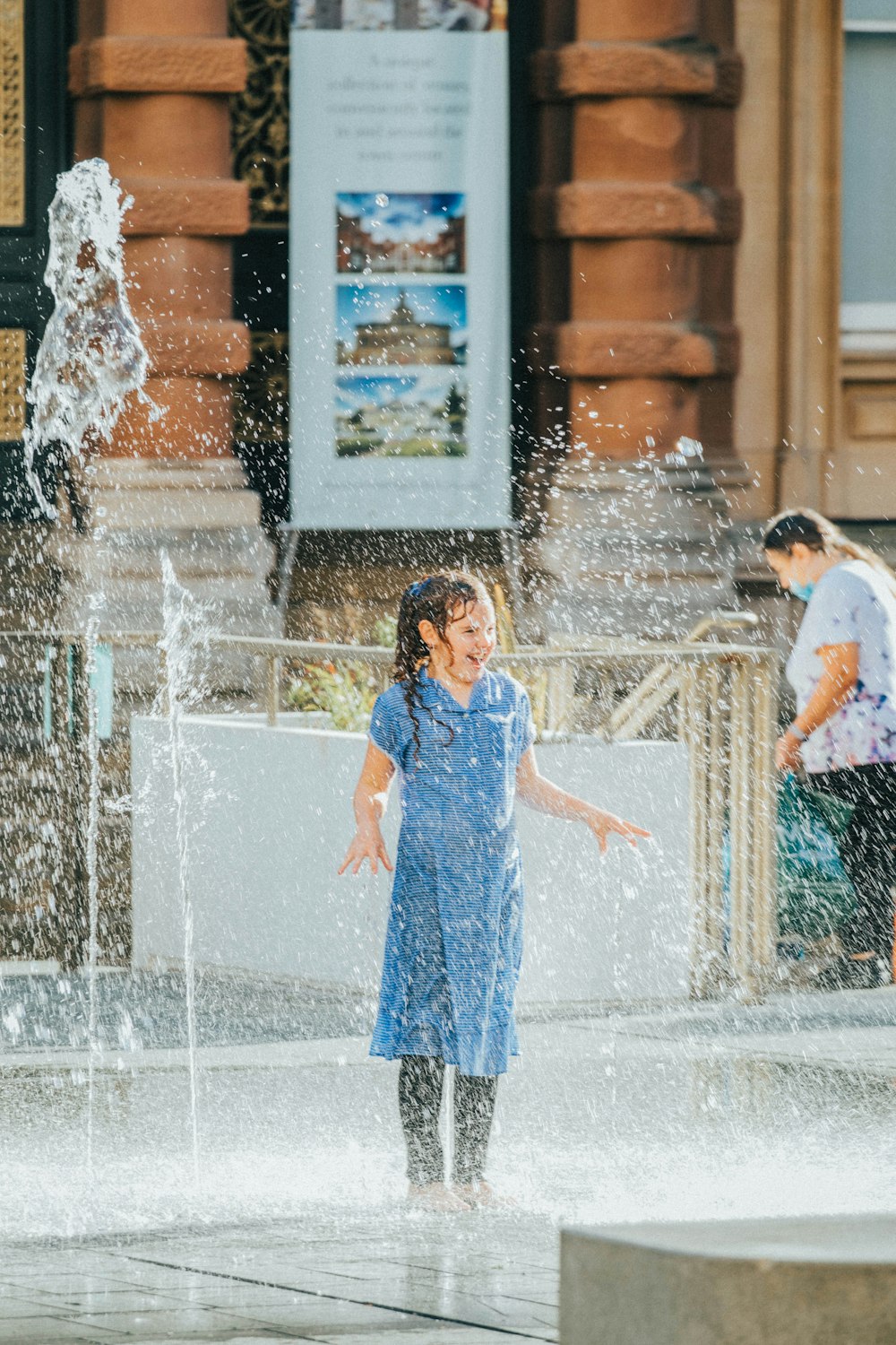 girl in blue dress standing on water fountain