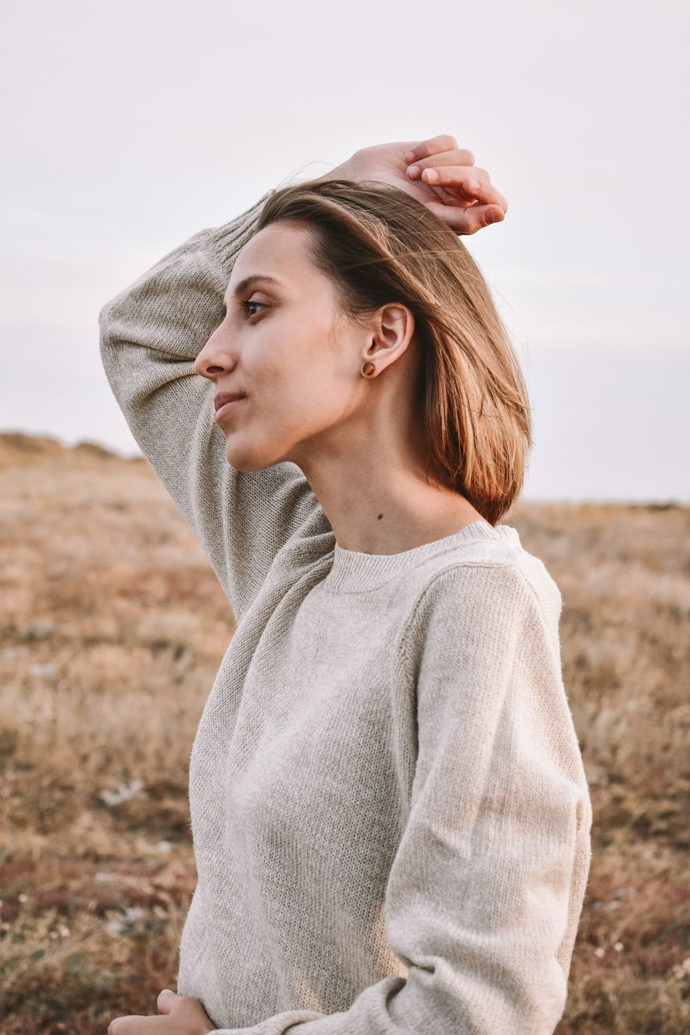 Mujer con suéter gris parada en un campo marrón durante el día