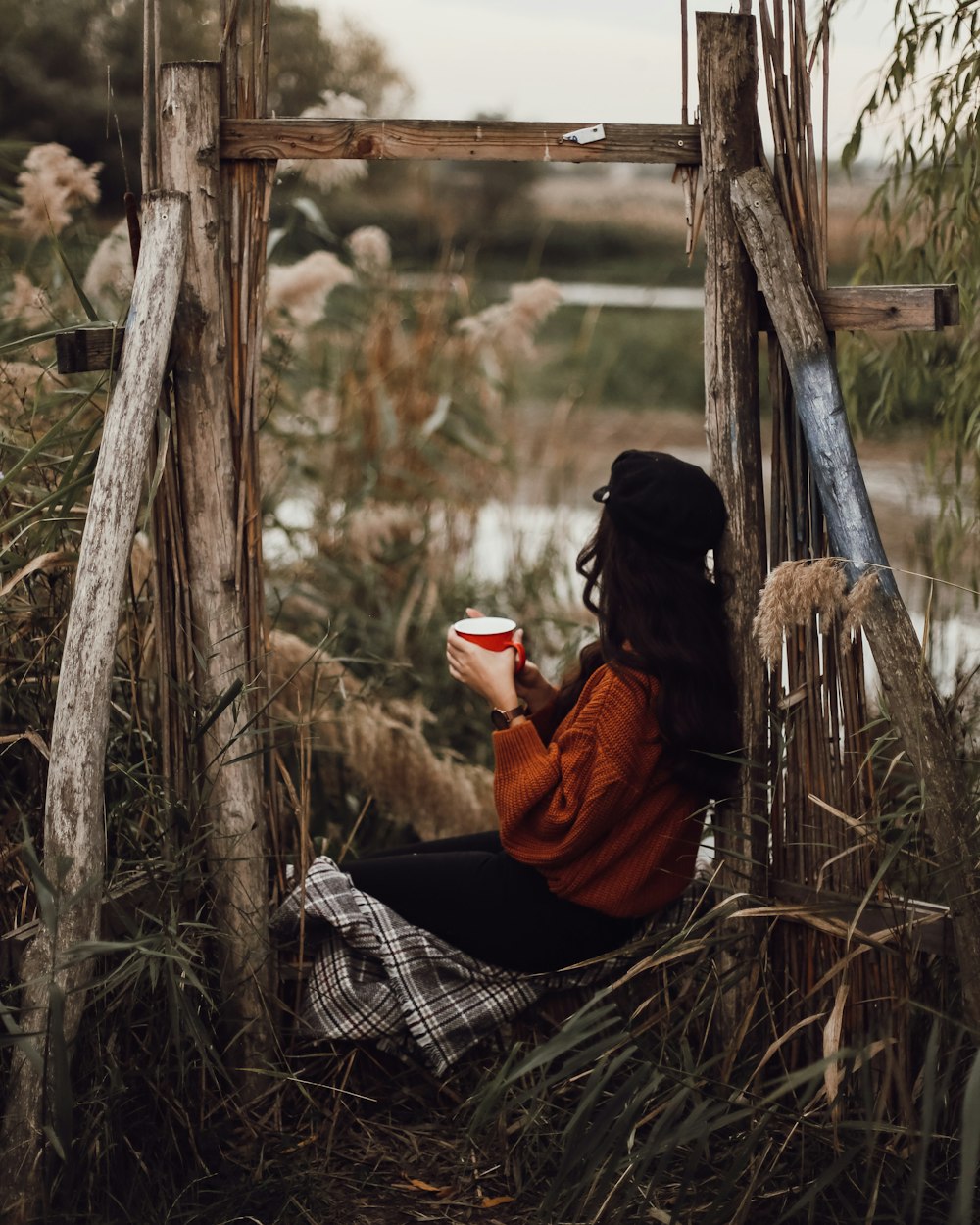 woman in black and red jacket sitting on brown wooden swing during daytime