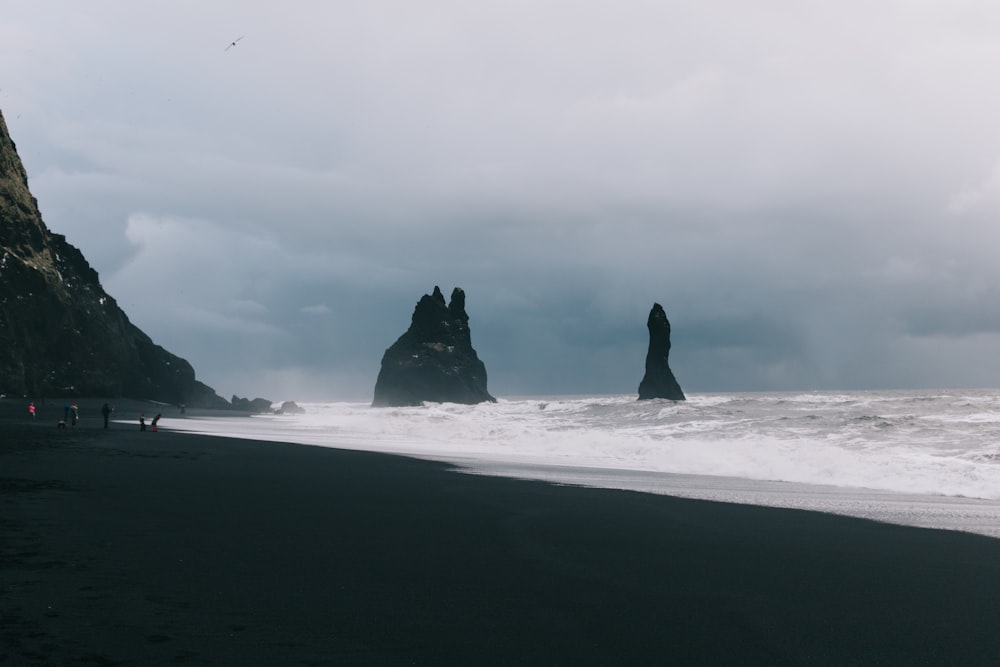 black rock formation on sea under white clouds during daytime