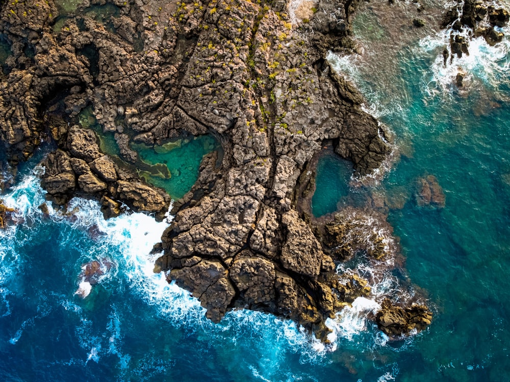 formação rochosa marrom e verde ao lado do mar azul durante o dia
