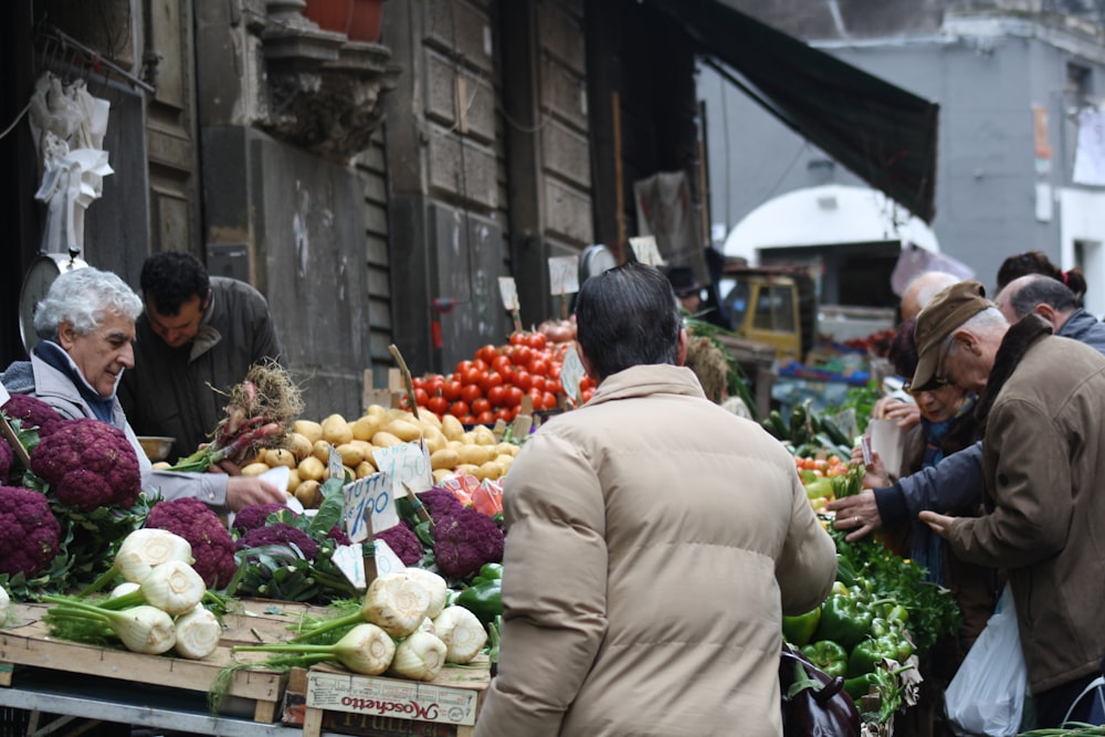 hombre con abrigo marrón de pie frente al puesto de frutas