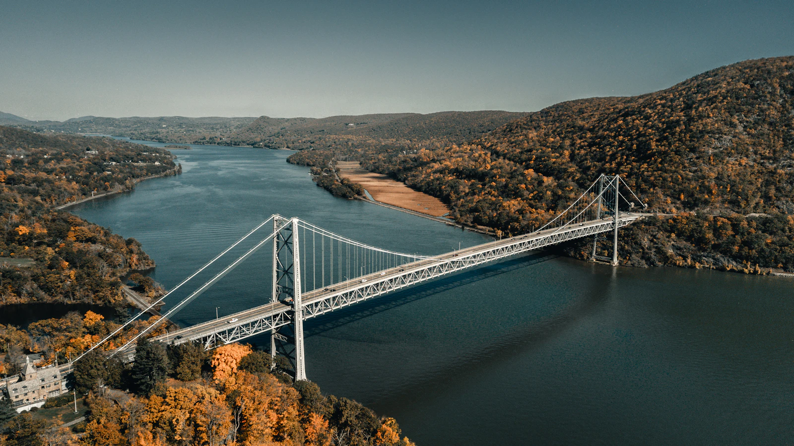 A suspension bridge spanning a river between autumn hills