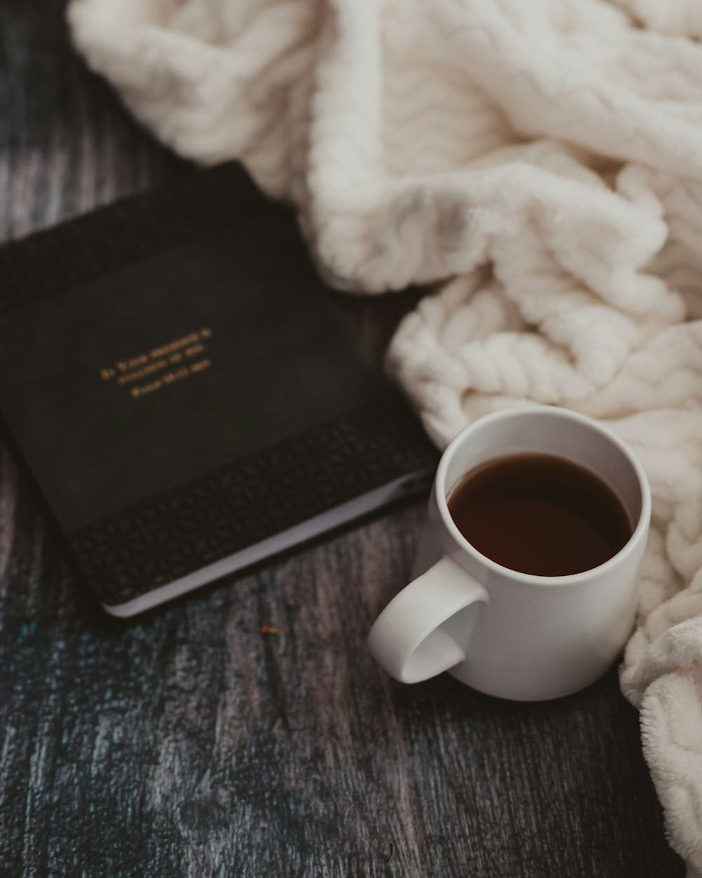 white ceramic mug beside black book