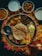 An array of traditional Indian dishes is arranged on a large round platter, surrounded by colorful flower petals. The platter includes flatbread, a dollop of butter, and various curries. Several small bowls containing creamy and spicy dishes are placed around the platter. A copper container is visible near the bottom right.