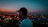 A vibrant shot of a woman rocking a Kocksure cap, city skyline glowing behind her at dusk.
