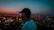 A vibrant shot of a woman rocking a Kocksure cap, city skyline glowing behind her at dusk.