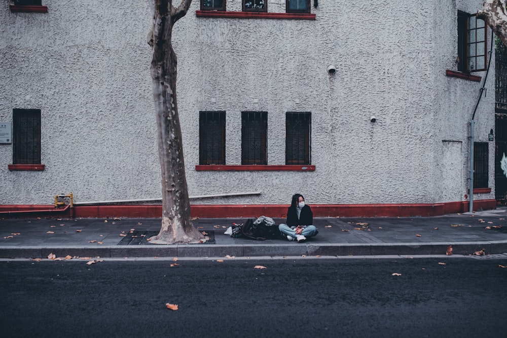 man in black jacket sitting on the sidewalk