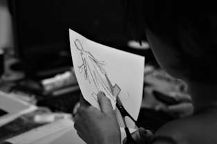 grayscale photo of woman holding pen writing on white paper