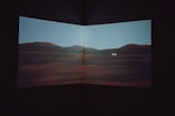 A dimly lit interior featuring a large screen or canvas displaying a scenic landscape of rolling hills under a clear sky with the word 'Sorry' written in the center.