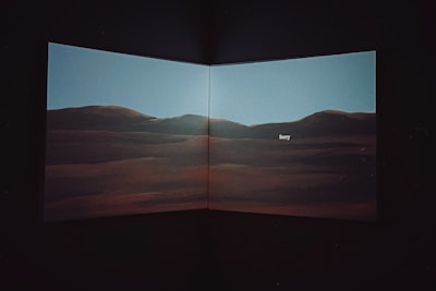 A dimly lit interior featuring a large screen or canvas displaying a scenic landscape of rolling hills under a clear sky with the word 'Sorry' written in the center.