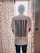 A person is standing with their back to the camera, wearing a white t-shirt that has the word 'INDIA' in large bold letters and 'Outcast' below it. The person is standing in front of a window with sheer, patterned curtains that have a dark blue dot design.