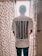 A person is standing with their back to the camera, wearing a white t-shirt that has the word 'INDIA' in large bold letters and 'Outcast' below it. The person is standing in front of a window with sheer, patterned curtains that have a dark blue dot design.