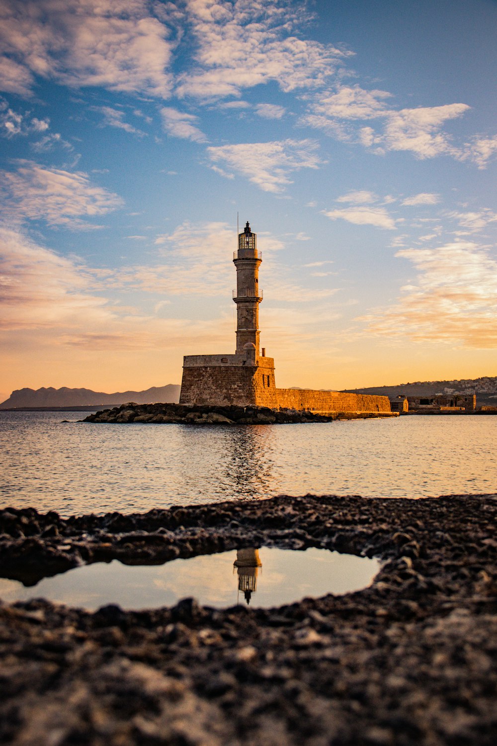 Faro marrón y blanco cerca del cuerpo de agua durante la puesta de sol