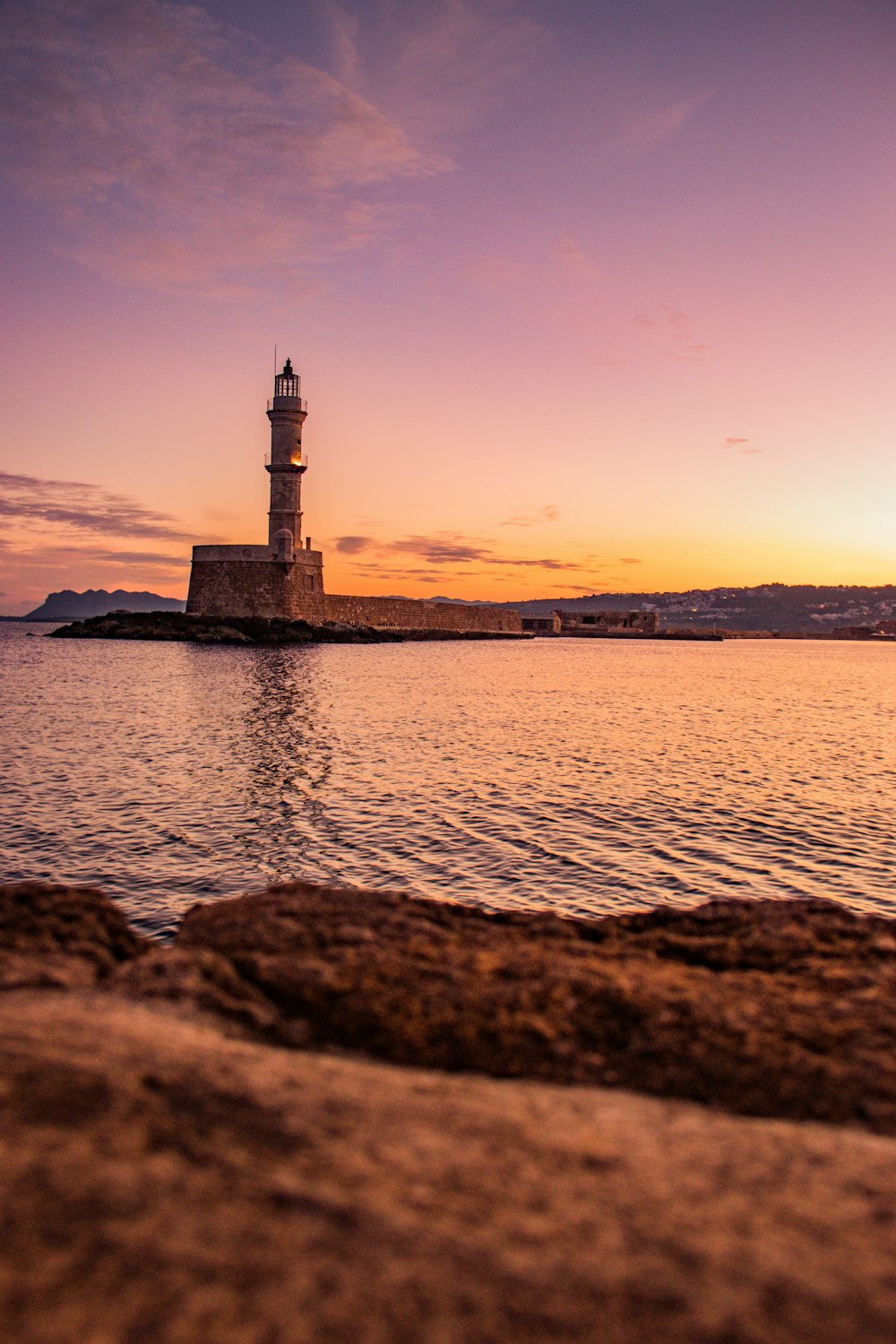 silhueta do farol perto do corpo de água durante o pôr do sol