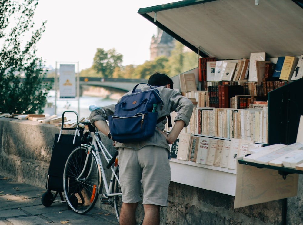 Homme en veste bleue et pantalon gris avec sac à dos bleu debout à côté du vélo pendant la journée