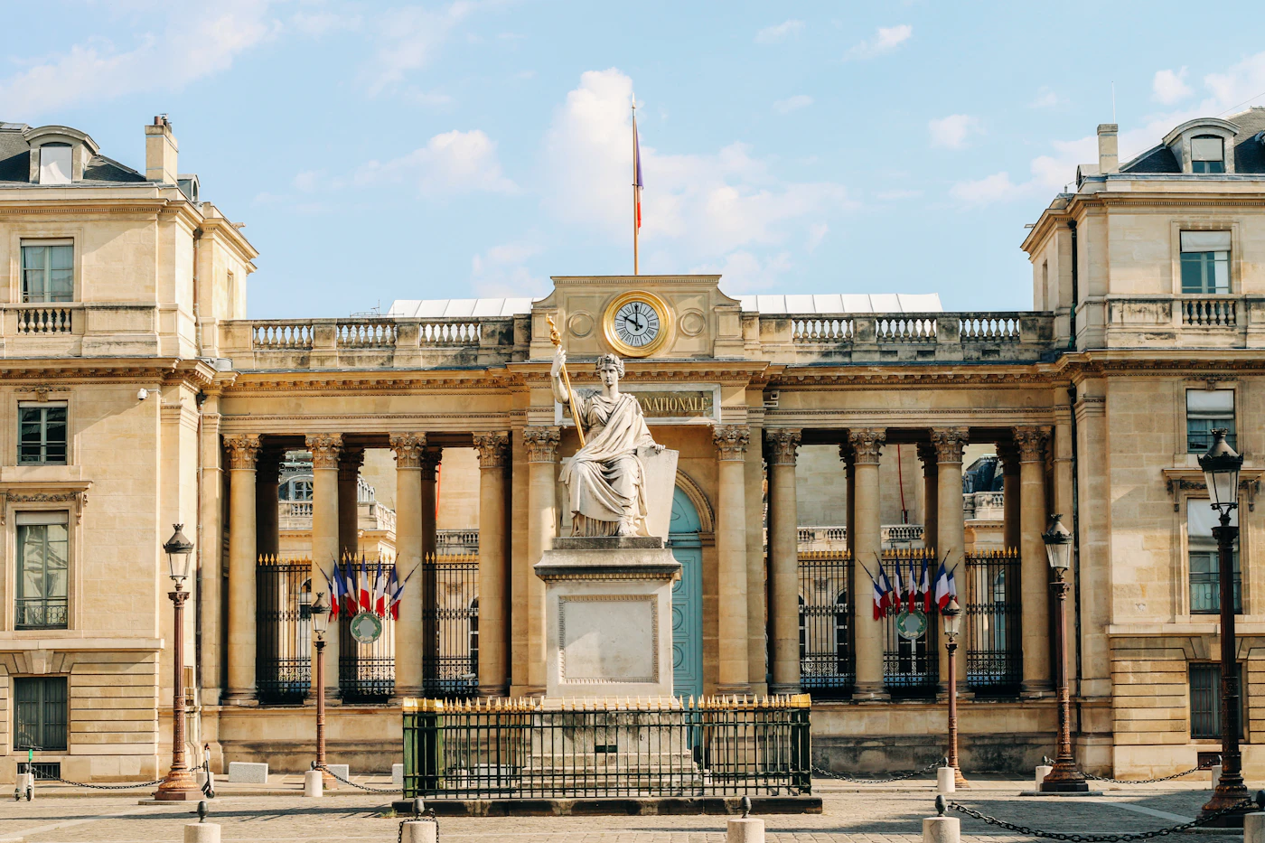 Colonnaded entrance of the Palais Bourbon in Paris, with a seated statue and French flags