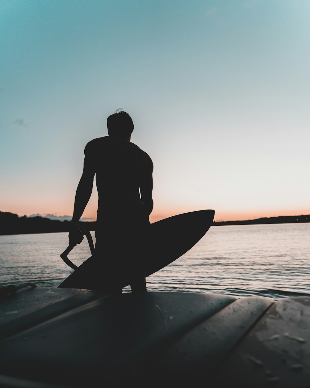 silhouette of man standing on surfboard during sunset