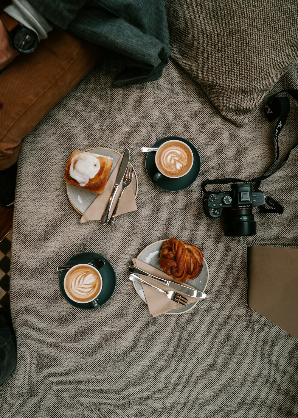 black dslr camera beside white ceramic mug and silver fork on gray textile