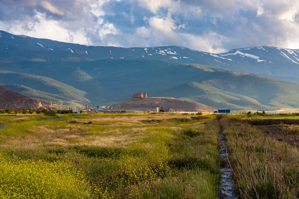 green grass field near mountain under white clouds during daytime