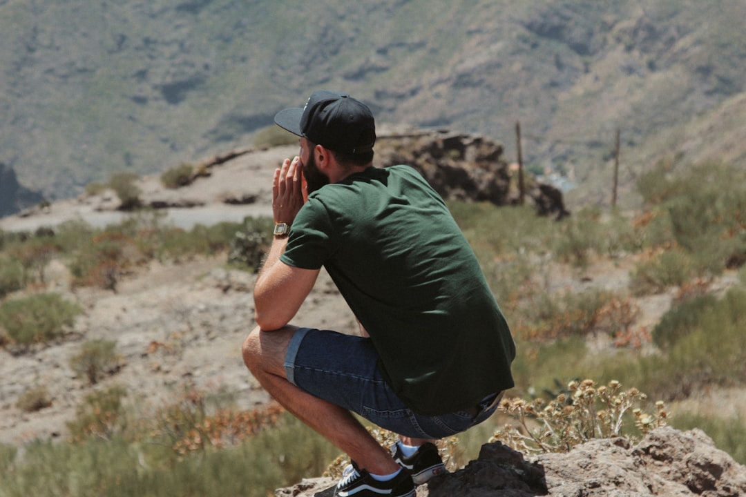 man in green t-shirt and blue denim shorts sitting on rock during daytime