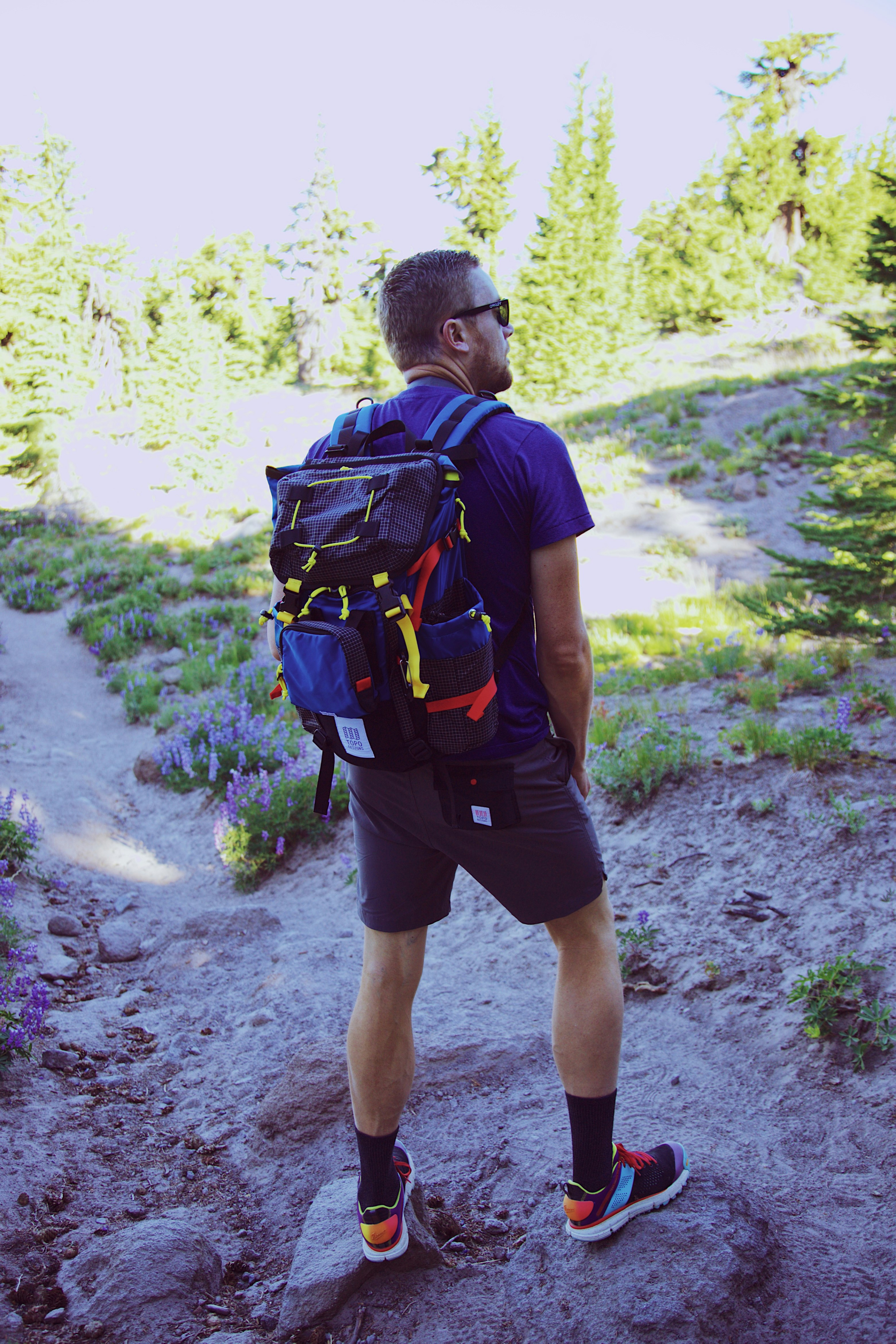 man in blue t-shirt and black shorts carrying black and blue hiking backpack walking on during