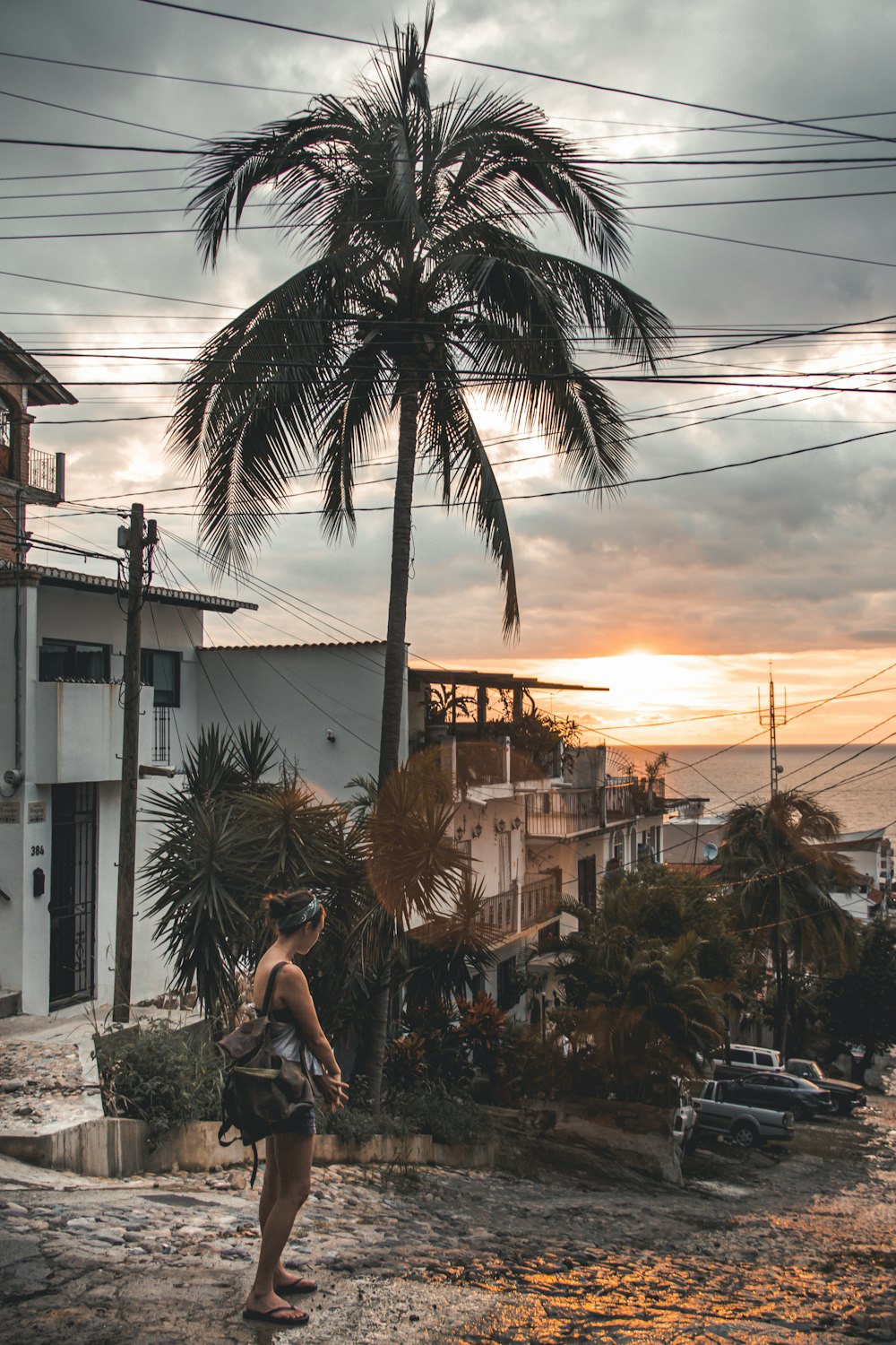 woman in white tank top sitting on concrete bench near palm tree during sunset