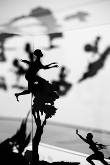 Silhouette images depict figures engaging in various dynamic poses, some appearing to be flying or climbing. The background is blurred, enhancing the contrast between the black figures and the lighter backdrop, giving a sense of motion and mystery.