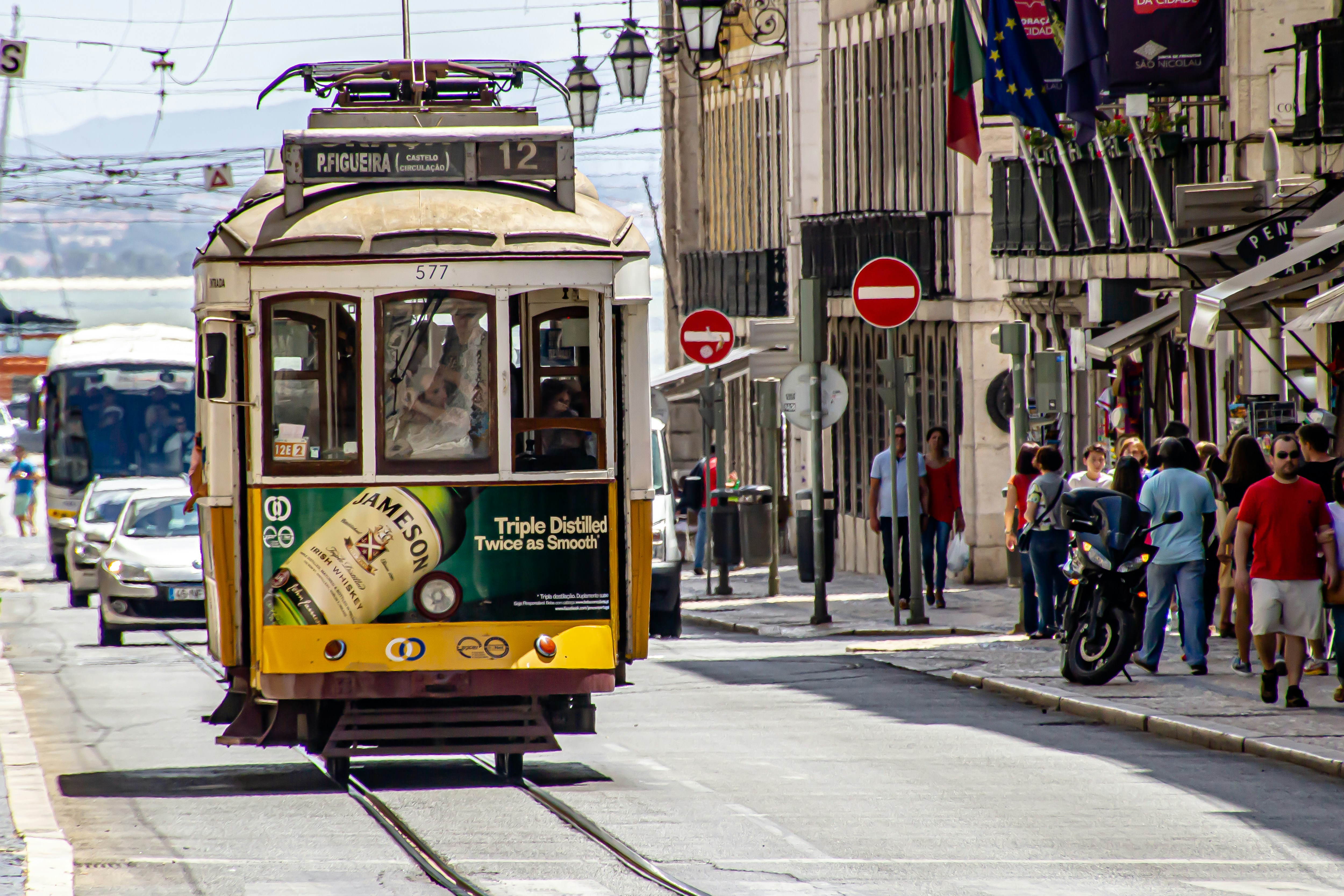 people walking on sidewalk near yellow tram during daytime