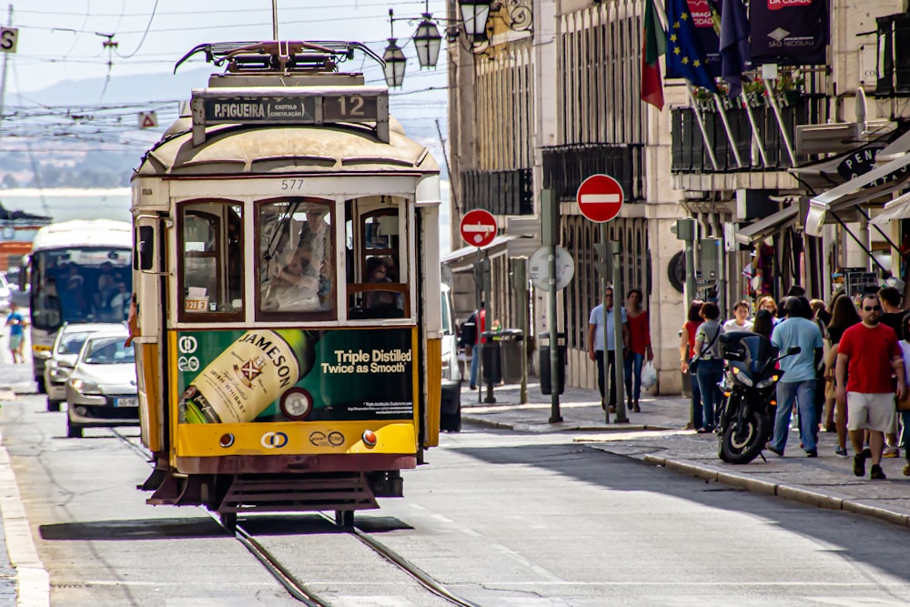 people walking on sidewalk near yellow tram during daytime