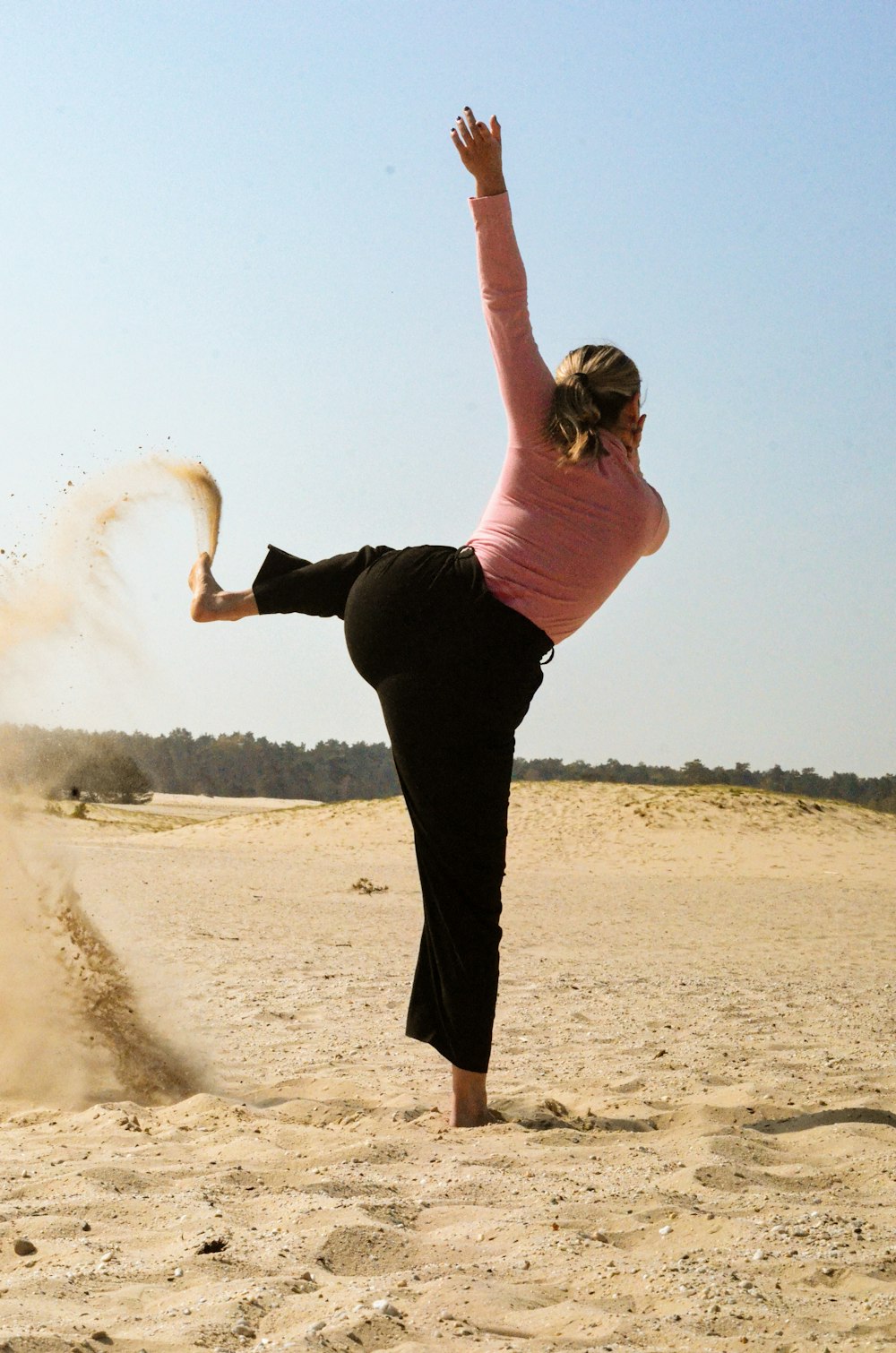 woman in pink shirt and black pants standing on brown sand during daytime