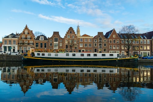 A large, modern houseboat moored along a canal in Haarlem with historic buildings in the background