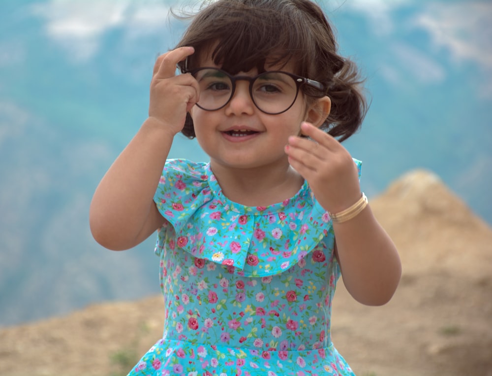 a little girl wearing glasses standing on top of a mountain