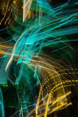 Bright, swirling lines of neon green and yellow light create an abstract pattern against a dark background. The movement of the lights suggests motion and energy.