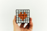 A hand is holding a complex Rubik's cube with a heart shape formed by orange squares in the center. The remaining squares are mostly white.