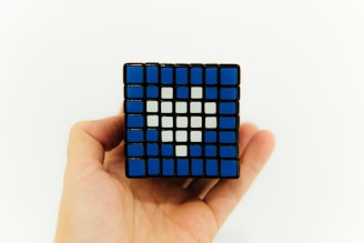 A hand holding a Rubik's cube that has been arranged to display a heart shape using a pattern of blue and white tiles.