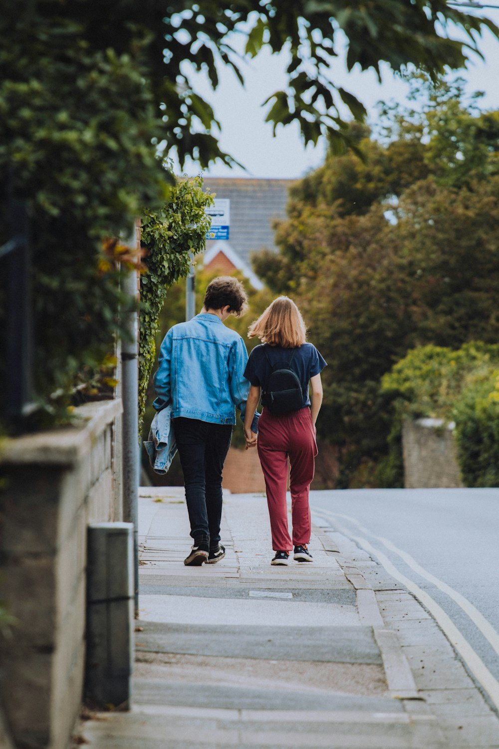 woman in blue jacket and red pants carrying black backpack walking on sidewalk during daytime