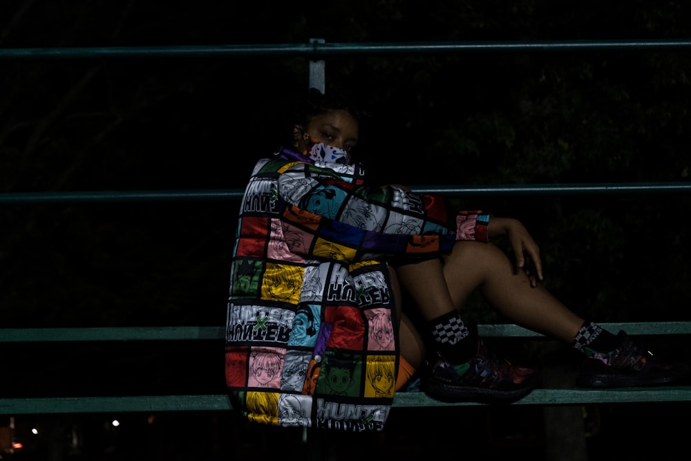 woman in blue yellow and red dress sitting on green metal bench