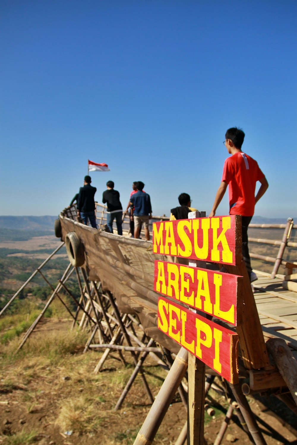 man in red t-shirt standing on brown wooden bridge