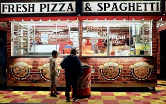 man in black jacket standing in front of food stall