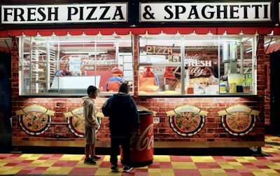 man in black jacket standing in front of food stall