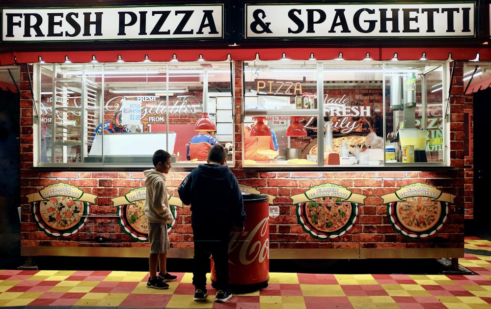 man in black jacket standing in front of food stall