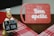 A cheerful chef figurine holds a sign with the message 'A DIETA JÁ ERA,' which translates to 'The diet is over.' In the background, a red cutting board features the phrase 'Bom apetite' with a chef's hat graphic. The scene includes a red and white checkered tablecloth.