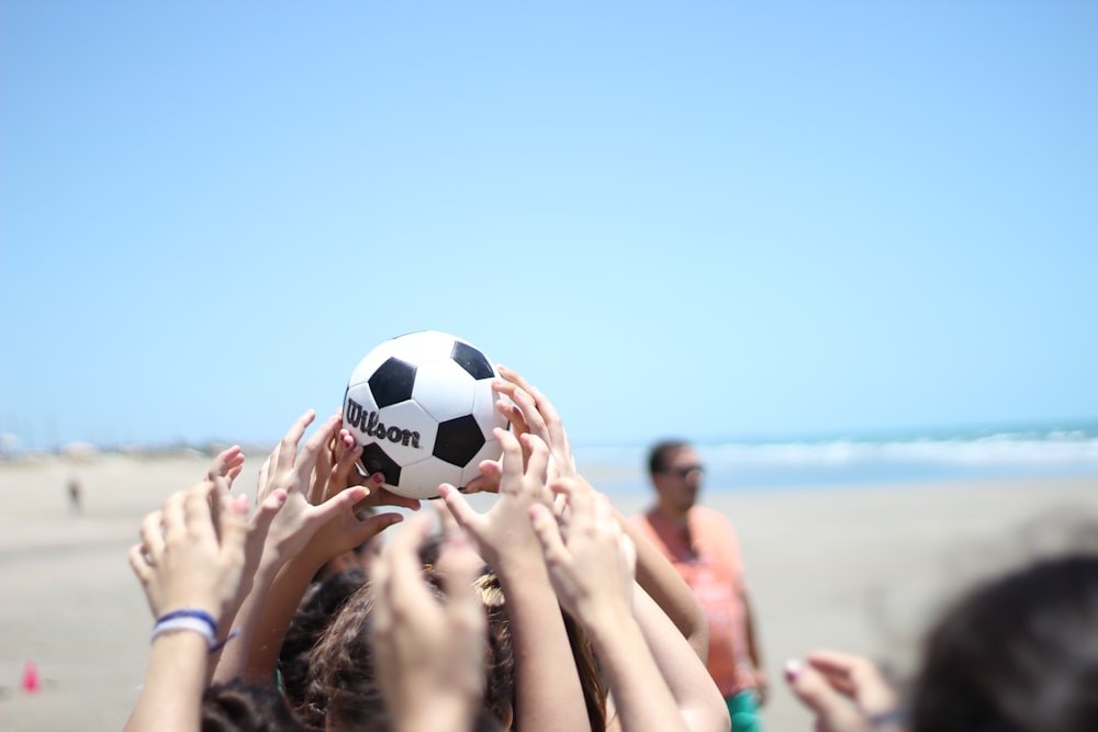 personas sosteniendo una pelota de fútbol blanca y negra bajo el cielo azul durante el día