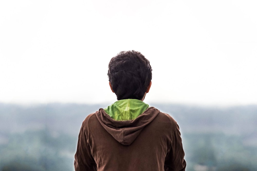 man in brown hoodie standing on green grass field during daytime